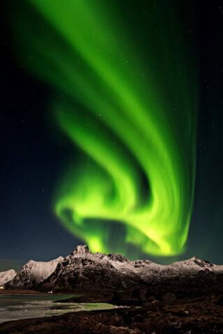 The image shows green aurora borealis lights swirling in the night sky over snow-covered mountains and a dark landscape in Norway.