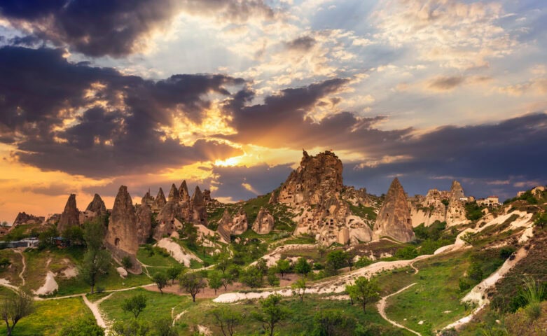 Rock formations and cave dwellings in Cappadocia, Turkey, with dramatic clouds and sunlight breaking through at sunset.