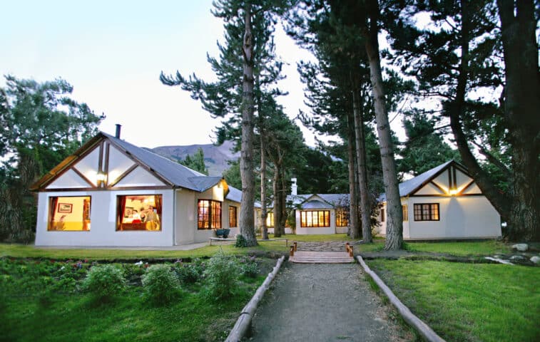 A peaceful house set in the woods of Argentina, with warm glowing lights from the windows, surrounded by trees and a dirt pathway leading to the entrance.