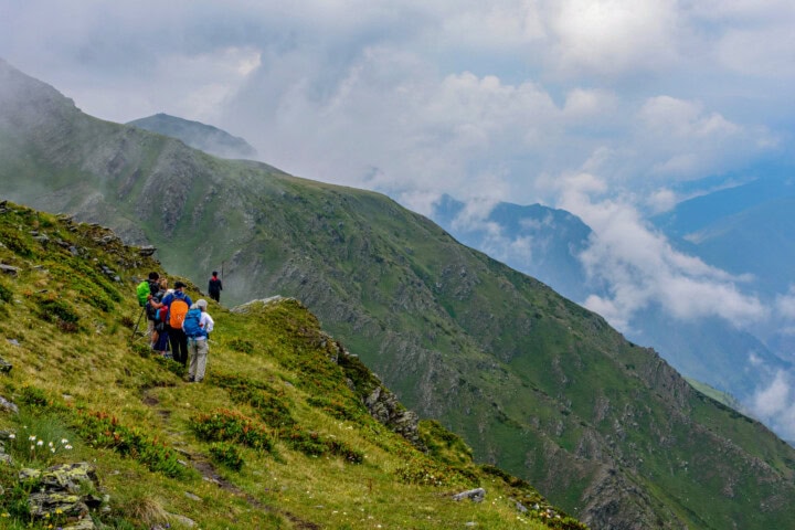 A group of five hikers stands on a grassy mountain trail in Georgia, overlooking a vast landscape with rolling mountains and scattered clouds, perfect for travel and tourism enthusiasts.