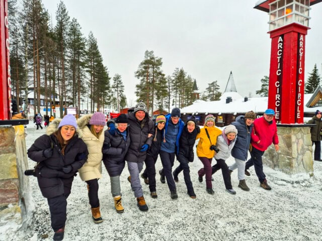 Group of tourists arm in arm stepping over Arctic Circle in Santa Claus Village, Rovaniemi Finland.