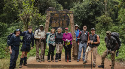 A group of hikers, ready to embark on their adventure, poses before the Kilimanjaro National Park sign at Lemosho Gate, surrounded by dense forest. Perfect for those following a beginner's guide to climbing Mount Kilimanjaro.