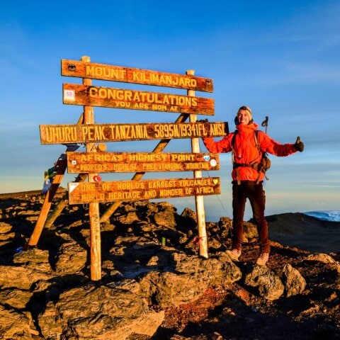 Hiker giving a thumbs up at the summit of Mount Kilimanjaro in Tanzania, Africa's highest point.