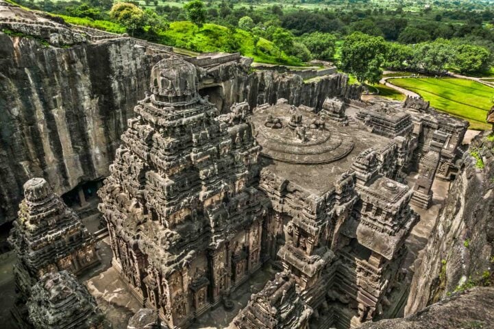 Aerial view of the ancient rock-cut Kailasa temple with intricate carvings, set against a backdrop of lush green trees and rolling hills, perfect for any traveler or guide looking to explore history and nature.