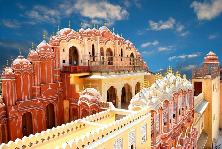 A vibrant, intricately designed palace with domes and spires against a partially cloudy sky invites you to embark on an architectural adventure. The structure features red and white hues with detailed lattice work, offering a rich tapestry for any guide to explore.