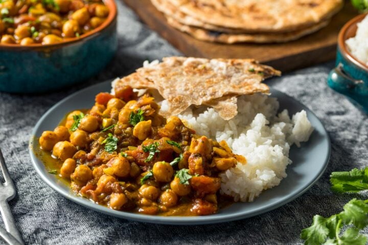 A plate of chickpea curry served with rice and flatbread, perfect after a long hike. Fresh cilantro garnishes the dish, adding a touch of color and flavor. Additional plates of food are visible in the background, making it feel like part of a culinary trip worth savoring.