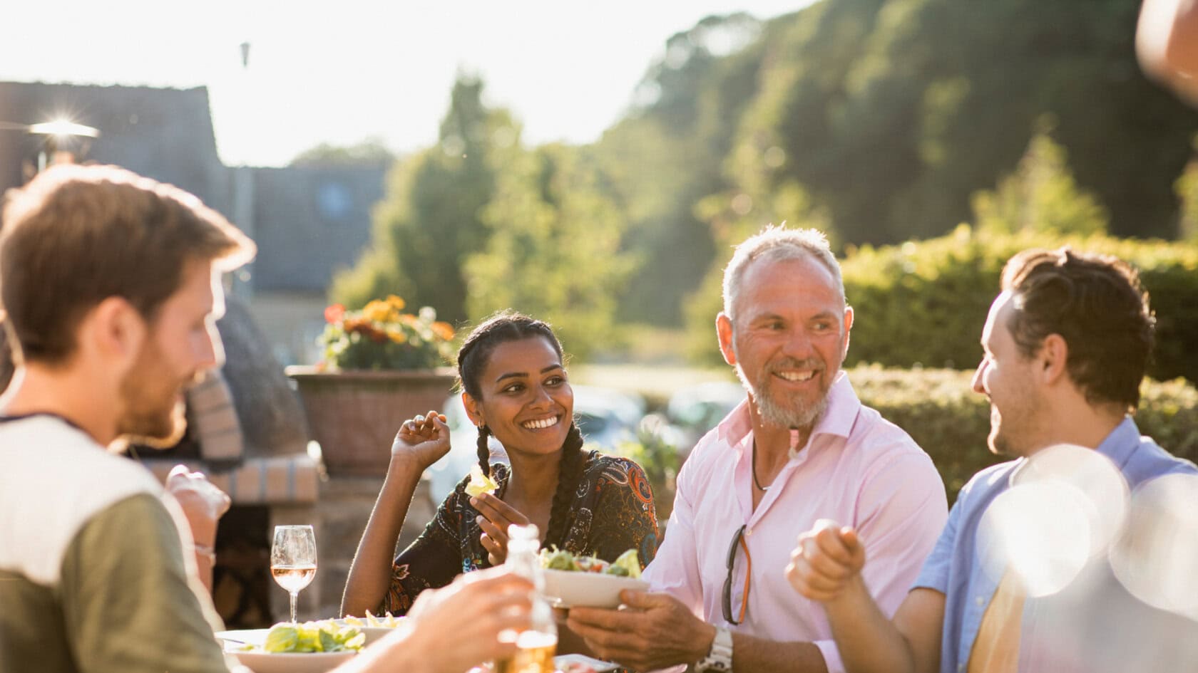 Friends sitting outside together eating and drinking. They are laughing together.