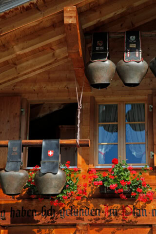 A wooden building with hanging cowbells above a window adorned with red flowers, capturing the essence of Swiss travel and evoking the charm of Switzerland's picturesque tourism spots.
