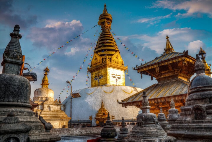 A detailed view of Swayambhunath Stupa in Kathmandu, Nepal, featuring its iconic eyes and surrounding structures under a partly cloudy sky with prayer flags representing the spirit of Nepal.