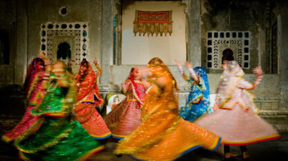 A group of women in colorful traditional attire perform a spinning dance in front of ornately decorated walls with arched windows—moments like these are not to miss in 2026.