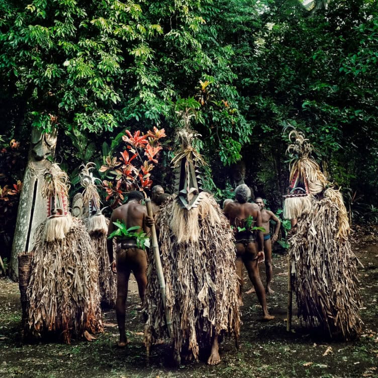 A group of people in a forest setting wear traditional costumes made of dried leaves and masks, with some participants adorned with green foliage—capturing moments not to miss in 2026.