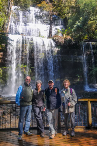 Four people standing on a wooden platform in front of a multi-tiered waterfall amidst a forested area in Tasmania.