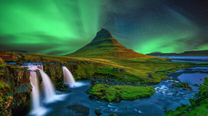 Northern lights illuminate the sky above Kirkjufell mountain and waterfall in Iceland, one of the best places for aurora adventures, against a backdrop of grassy landscapes and flowing water.