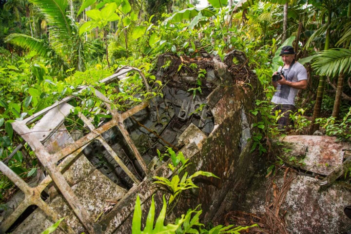 Photographer examines overgrown airplane wreckage in the dense jungle of Palau, a hidden gem for travel enthusiasts.